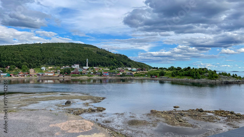  A small northern village on the White Sea coast with colorful houses, a church, and forested hills under a dramatic sky — peaceful and remote coastal life.