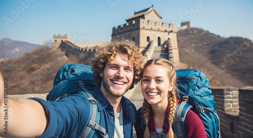 Smiling young couple taking selfie at Great Wall of China wearing backpacks sunny day travel adventure