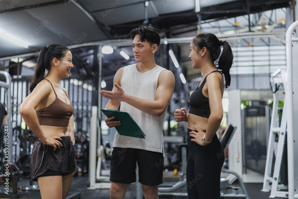 Fototapeta premium Personal trainer explaining training program to two women in gym