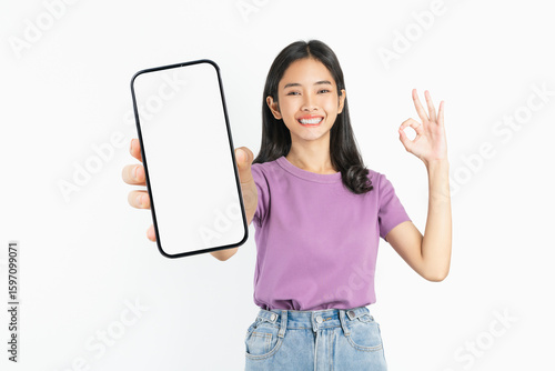 Smiling asian woman holding smartphone with blank screen and shows ok sign on white background