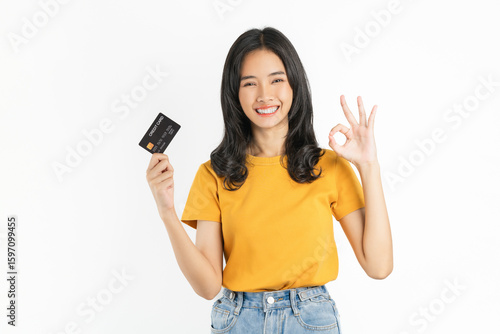 Smiling asian woman holding credit card and shows ok sign on white background.