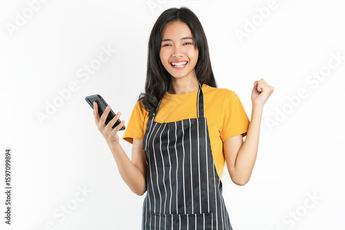 Happy Asian woman owner in black apron standing with holding smartphone on white background.