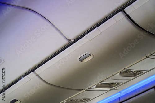 Konstfotografi Captured from below, the streamlined interior showcases the overhead compartment with its sleek design, complemented by individual air vents and blue lighting, symbolizing travel and comfort
