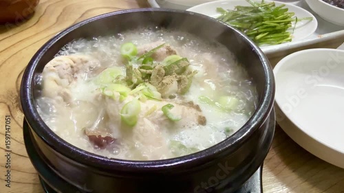 Samgyetang served hot in ttukbaegi or the black hot pot with various side dish on the table in a restaurant