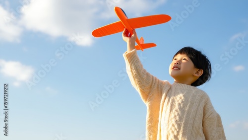 A child holds an orange toy airplane high above their head gazing up with excitement