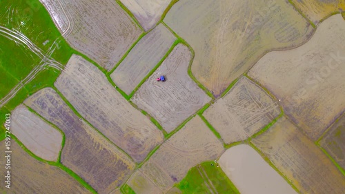 4K Drone Footage of Tractor Ploughing a Rice Field During Monsoon Farming in India - High-resolution aerial video showing a red tractor ploughing a muddy rice field during the wet farming season. 