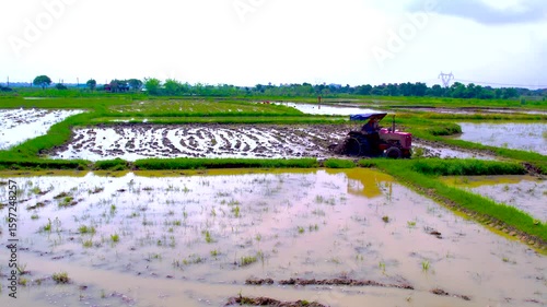 4K Drone Footage of Tractor Ploughing a Rice Field During Monsoon Farming in India - High-resolution aerial video showing a red tractor ploughing a muddy rice field during the wet farming season. 