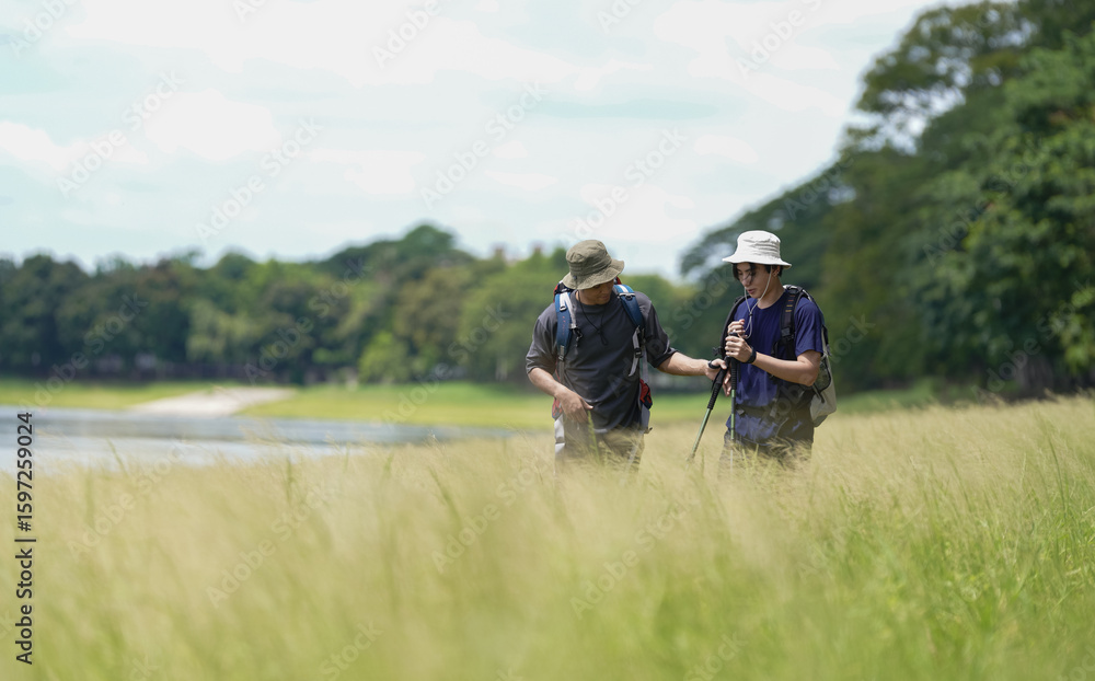 Obraz premium Happy tourist hiking walking together over grassland of the plains. Active young adult man trekking through nature grass field over lowland in rural trail. Portrait of real people in peaceful meadow.