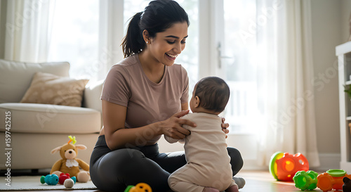 A smiling Indian mother sits on the floor with her baby, who is learning to sit up, surrounded by colorful toys in a bright and comfortable living room