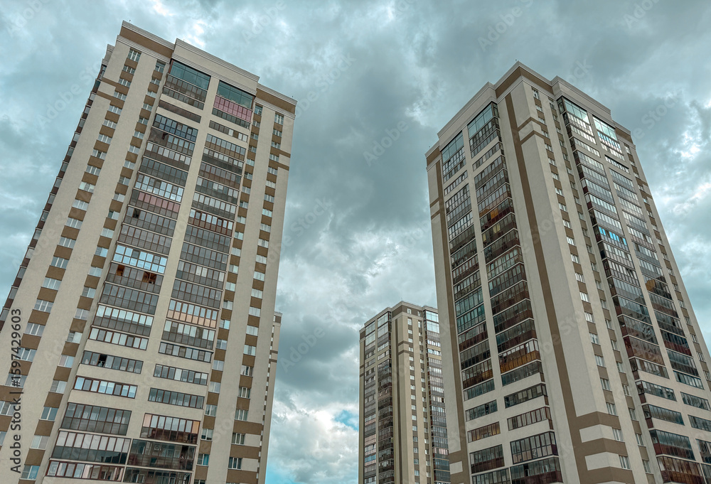 Naklejka premium Three tall buildings with many windows and a cloudy sky in the background