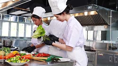 Female chef teaches cooking to two teenage girls, learning how to select vegetables, preserve food and cook, everyone wears black gloves in cooking class.