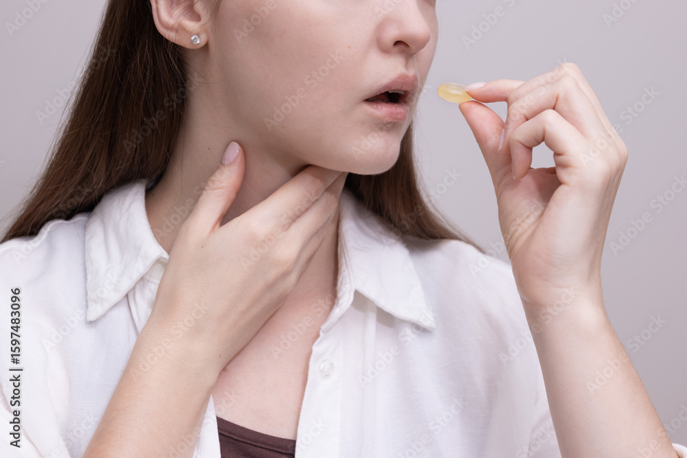 Woman holding throat and preparing to take lozenge for sore throat relief. Concept of cold treatment, throat pain, and seasonal illness. Woman holding throat and preparing to take lozenge for sore throat relief. Concept of cold treatment, throat pain, and seasonal illness.