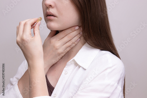 Female experiencing sore throat preparing to take lozenge for sore throat relief.  Concept of cold treatment, throat pain, and seasonal illness.
