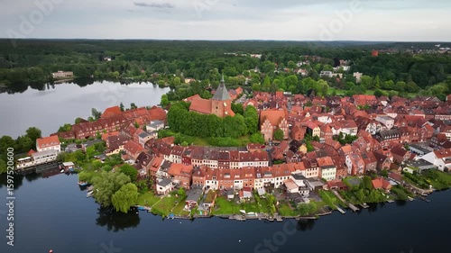 Aerial orbit of the old town of Mölln, the Eulenspiegel town,  with red rooftops, half-timbered houses, and St. Nicolai Church on a hill, surrounded by lakes.