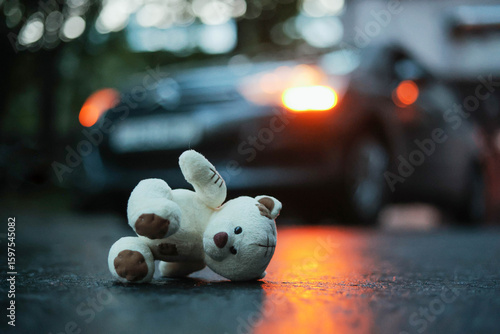 Teddy bear lying on a wet road and car with blinker in the background. Car accident.