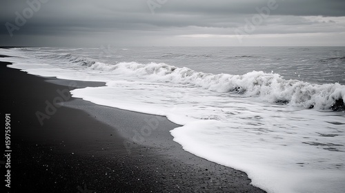 Dark sand beach meets foamy waves on a gray overcast day