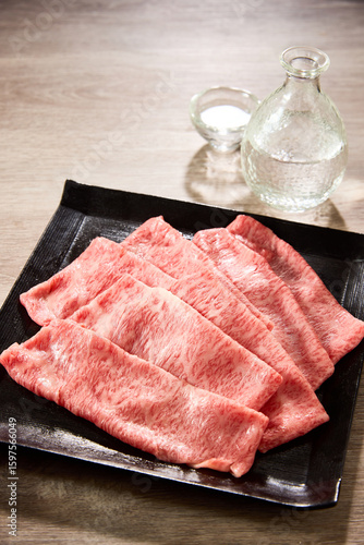 黒毛和牛の霜降りスライス肉を黒い角皿に美しく盛り付け、日本酒の徳利と盃を添えた高級感あふれる和食の食卓シーン。すき焼きやしゃぶしゃぶに最適な素材。
