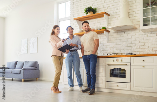 Принти на полотні Female broker giving tour for family couple, showing spacious house, demonstrating kitchen