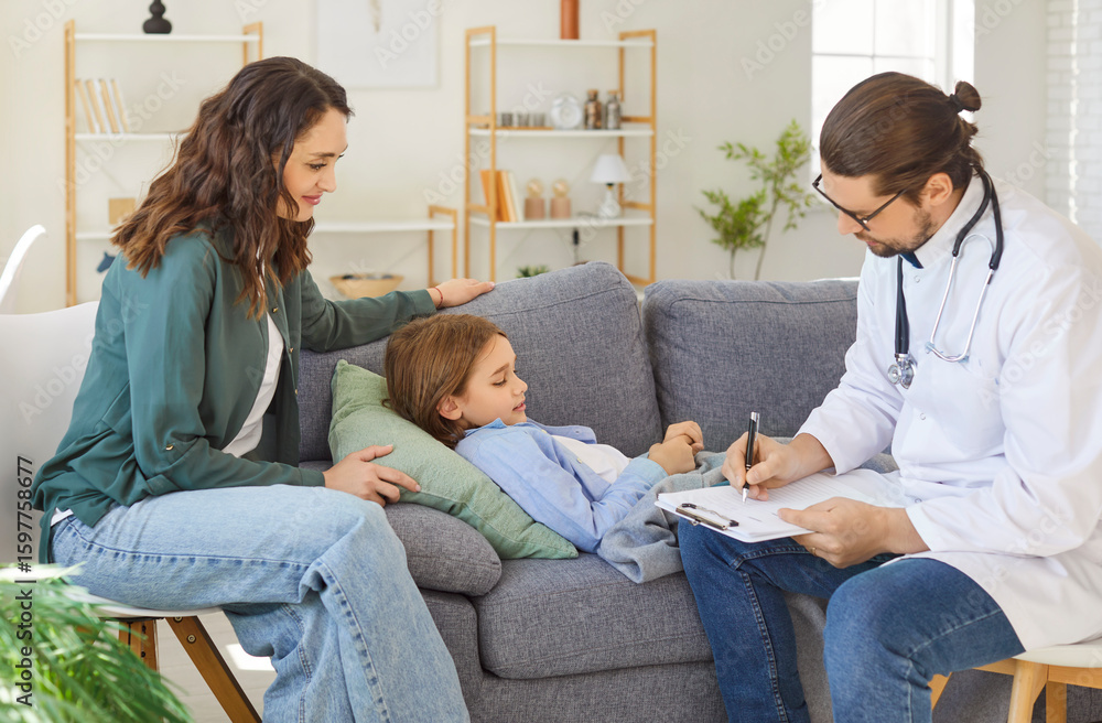 Male doctor writing notes during home visit while little child resting on sofa with her concerned mother nearby. Focused pediatrician writing prescription or diagnosis after medical health checkup. Male doctor writing notes during home visit while little child resting on sofa with her concerned mother nearby. Focused pediatrician writing prescription or diagnosis after medical health checkup.