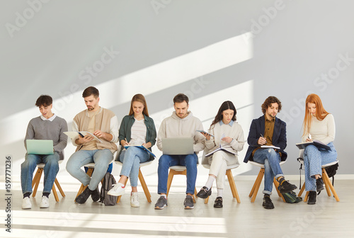 Young people with backpacks, notebooks and laptops sitting in lobby. Male and female fresher or graduate students waiting in line for job interview to use youth internship staff recruiting opportunity