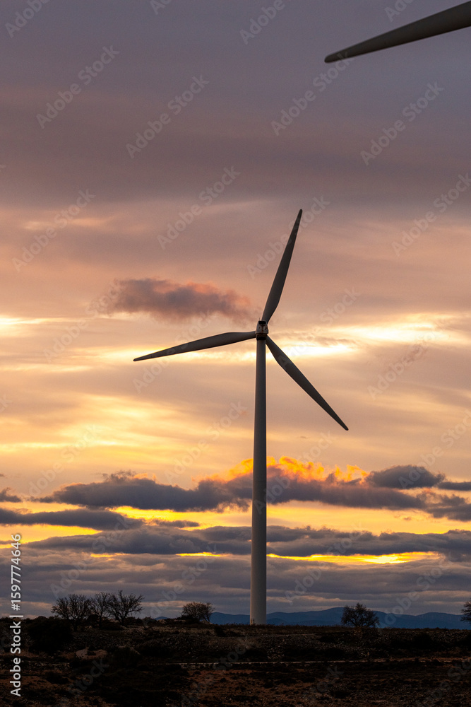 Clean energy windmills rising above arid terrain in Zaragoza, Spain, with evening clouds and sunset hues, highlighting renewable infrastructure and ecological power transformation in Europe. Clean energy windmills rising above arid terrain in Zaragoza, Spain, with evening clouds and sunset hues, highlighting renewable infrastructure and ecological power transformation in Europe.