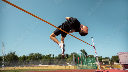 Foto Athlete executes high jump at an outdoor sports venue beneath a blue sky
