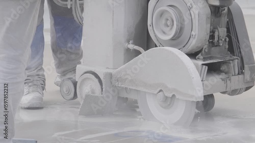 Worker cutting concrete floor with large industrial saw, captured from side angle. Dust and debris fill the scene. Filmed at airport construction site in Turkey. Ideal for industry and construction.