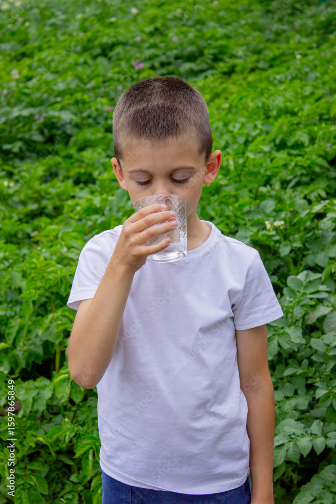 Boy drinking water from a glass against a background of nature Boy drinking water from a glass against a background of nature