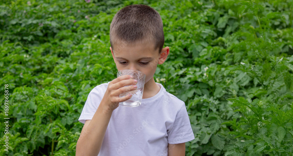 Boy drinking water from a glass against a background of nature Boy drinking water from a glass against a background of nature