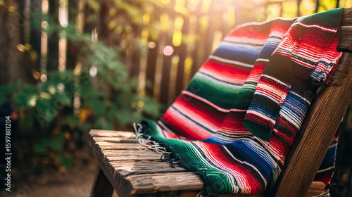 A traditional embroidered serape poncho in bold stripes of red, green, and white, draped over a rustic wooden chair with soft sunlight.
