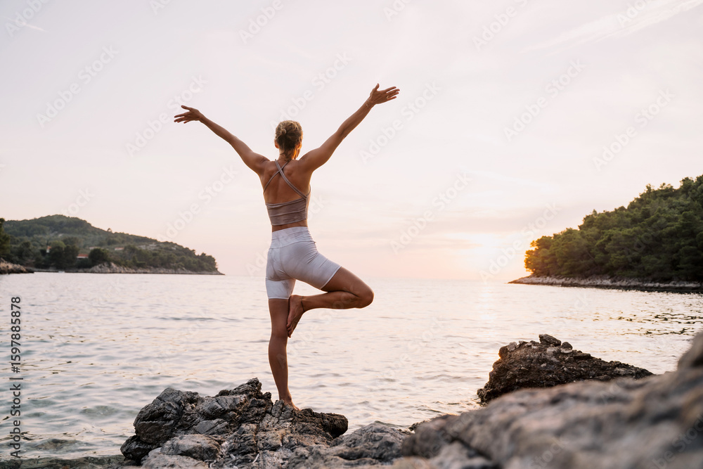 Obraz premium Woman practicing yoga at seaside at sunset or sunrise. Holistic Health and Mental Well-Being.