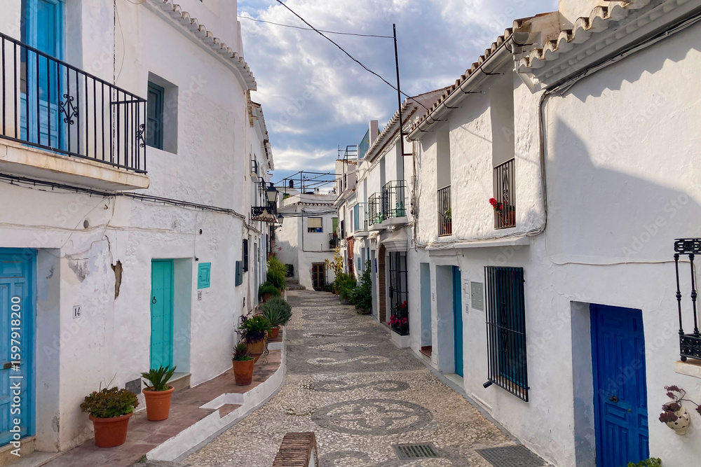 Fototapeta premium FRIGILIANA, SPAIN - MAY 10, 2025: A peaceful walk through the charming narrow streets, surrounded by whitewashed houses and colorful flowers in Frigiliana, Spain