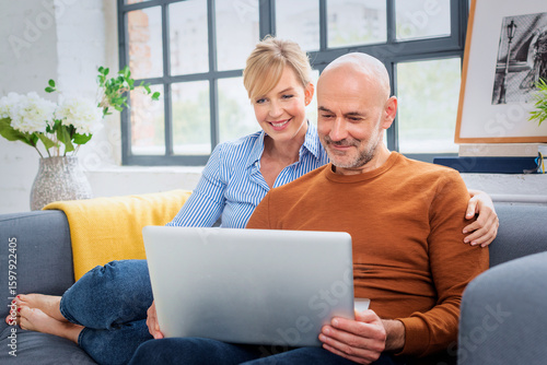 Middle aged couple using laptop together in her modern home