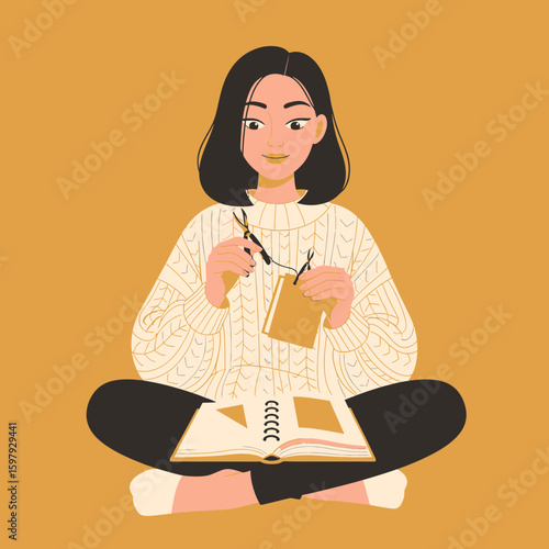 A young woman sits cross-legged, crafting with scissors, string, and paper, working on a scrapbook.