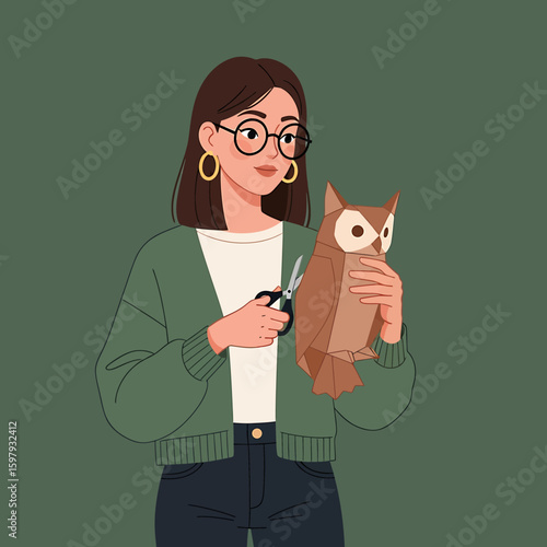 A woman with glasses and a green cardigan is cutting paper with scissors, holding a brown paper owl.