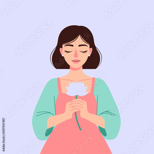 Woman with short brown hair, eyes closed, holding a white flower in her hands, wearing a pink dress and green cardigan.