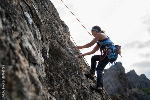 Slika na platnu Middle aged female climber removing quickdraw from bolt during top rope descent,