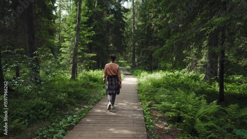 Walk inside fabulous forest in summer, one woman tourist strolling on pathway. Carefree female traveler hiking and admiring tall coniferous trees, eco-tourism in summer weekend, discover new location