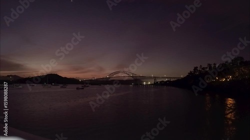 Sunset timelapse of the Bridge of the Americas in Panama with ships anchored in calm waters under a twilight sky.