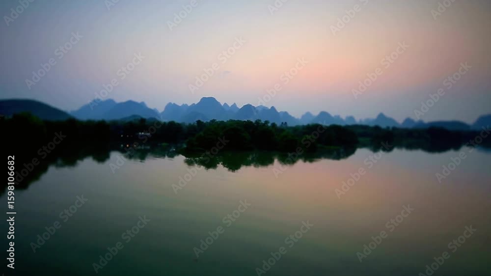 A tranquil lake reflects the silhouette of karst mountains at sunset A tranquil lake reflects the silhouette of karst mountains at sunset