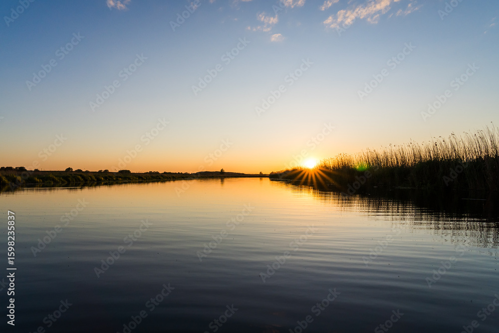 Obraz premium Sunset over the Trebel River with Sun Rays Shining through the Reeds