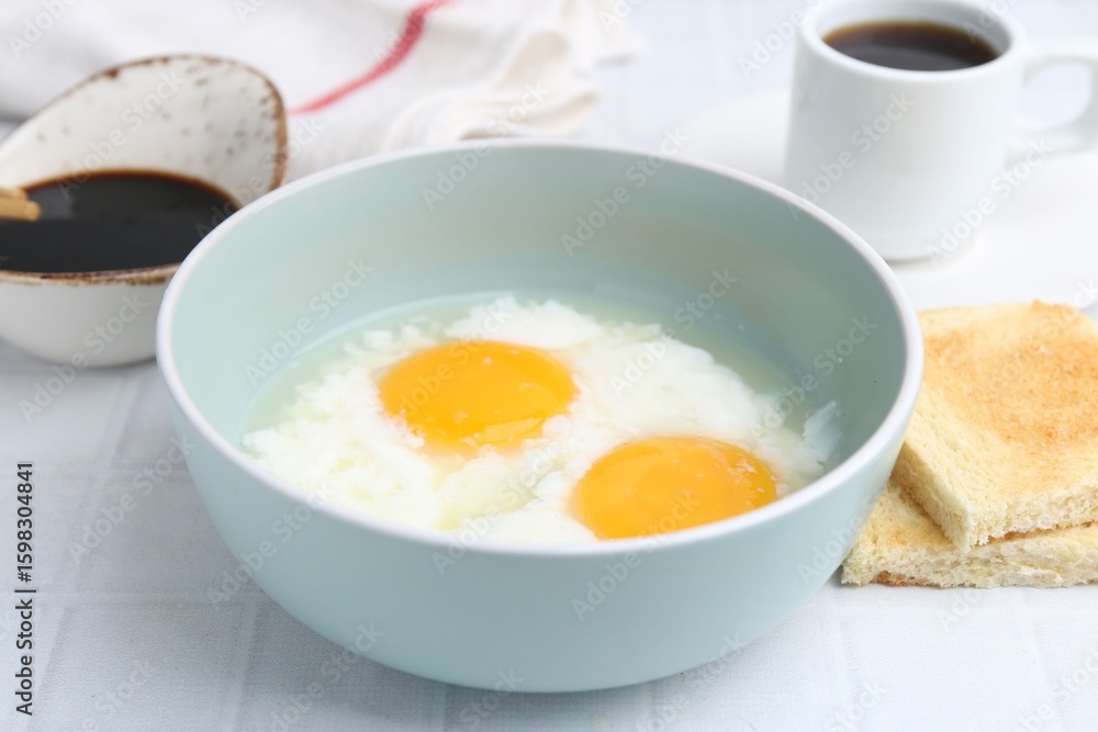 Traditional asian breakfast with half-boiled eggs in bowl, soy sauce, bread and coffee on white tiled table, closeup Traditional asian breakfast with half-boiled eggs in bowl, soy sauce, bread and coffee on white tiled table, closeup
