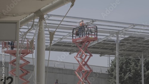 Workers installing solar panel structure using forklifts at a renewable energy site. Captured at solar canopy construction in Turkey. Ideal for sustainability, teamwork, and industrial process themes.