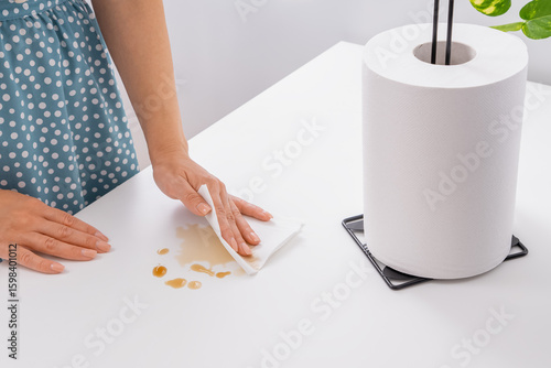A woman in the kitchen wipes spilled tea or coffee on the table with a white paper napkin. Side and top view. Horizontal photo.