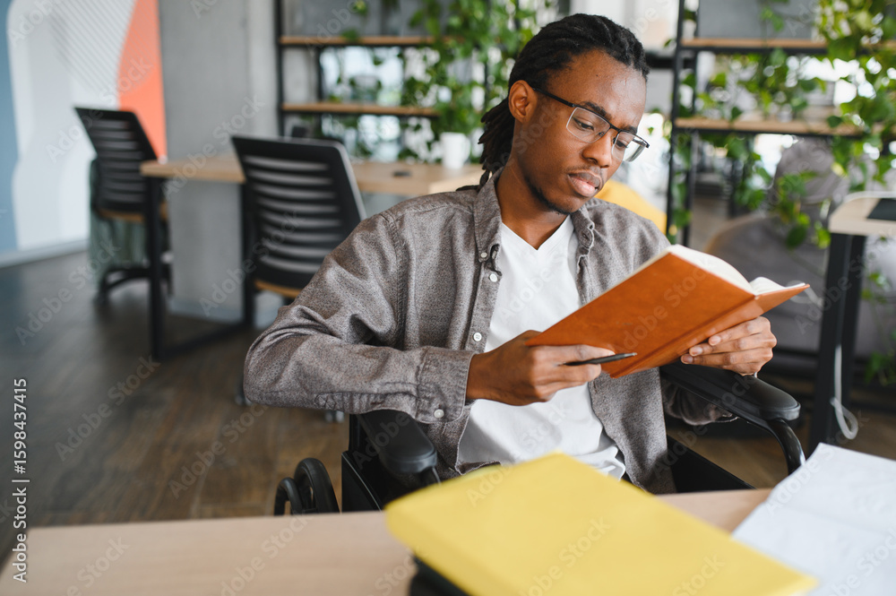 Focused african american student in wheelchair reading a book in modern office Focused african american student in wheelchair reading a book in modern office