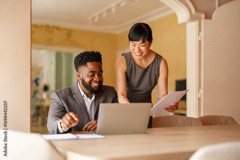 Smiling business professionals with documents and laptop discussing project at desk in modern office Smiling business professionals with documents and laptop discussing project at desk in modern office