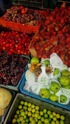 Colorful assortment of tropical fruits including guavas, limes, rambutans, bananas, grapes, and plums on display at a local market stall in Munnar, Kerala, India.