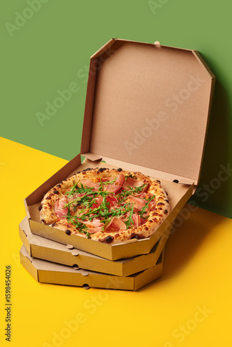 Delicious pizza with prosciutto and arugula in a delivery box on colorful background