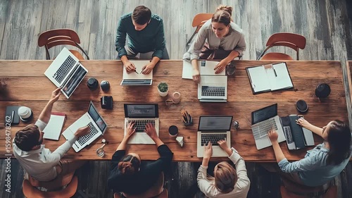Team collaboratively works on laptops, seated around a rustic wooden conference table