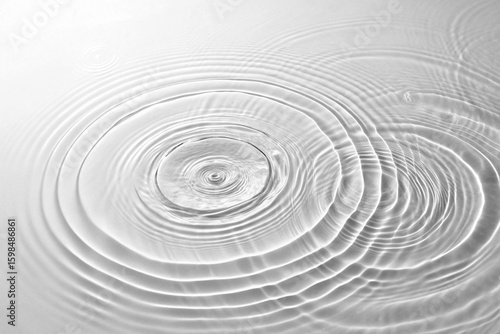 A serene and minimalist view of gentle concentric water waves expanding from two impact points, creating an elegant interference pattern on a clear surface.